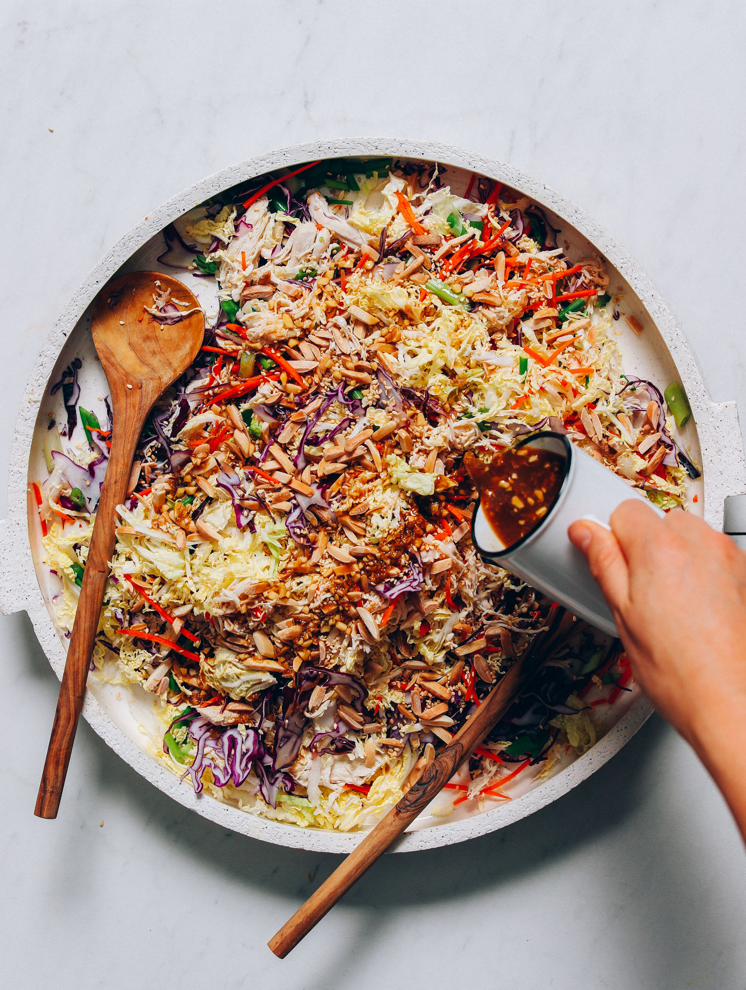 Pouring Sesame Ginger dressing onto a large platter of our Crunchy Cabbage Slaw