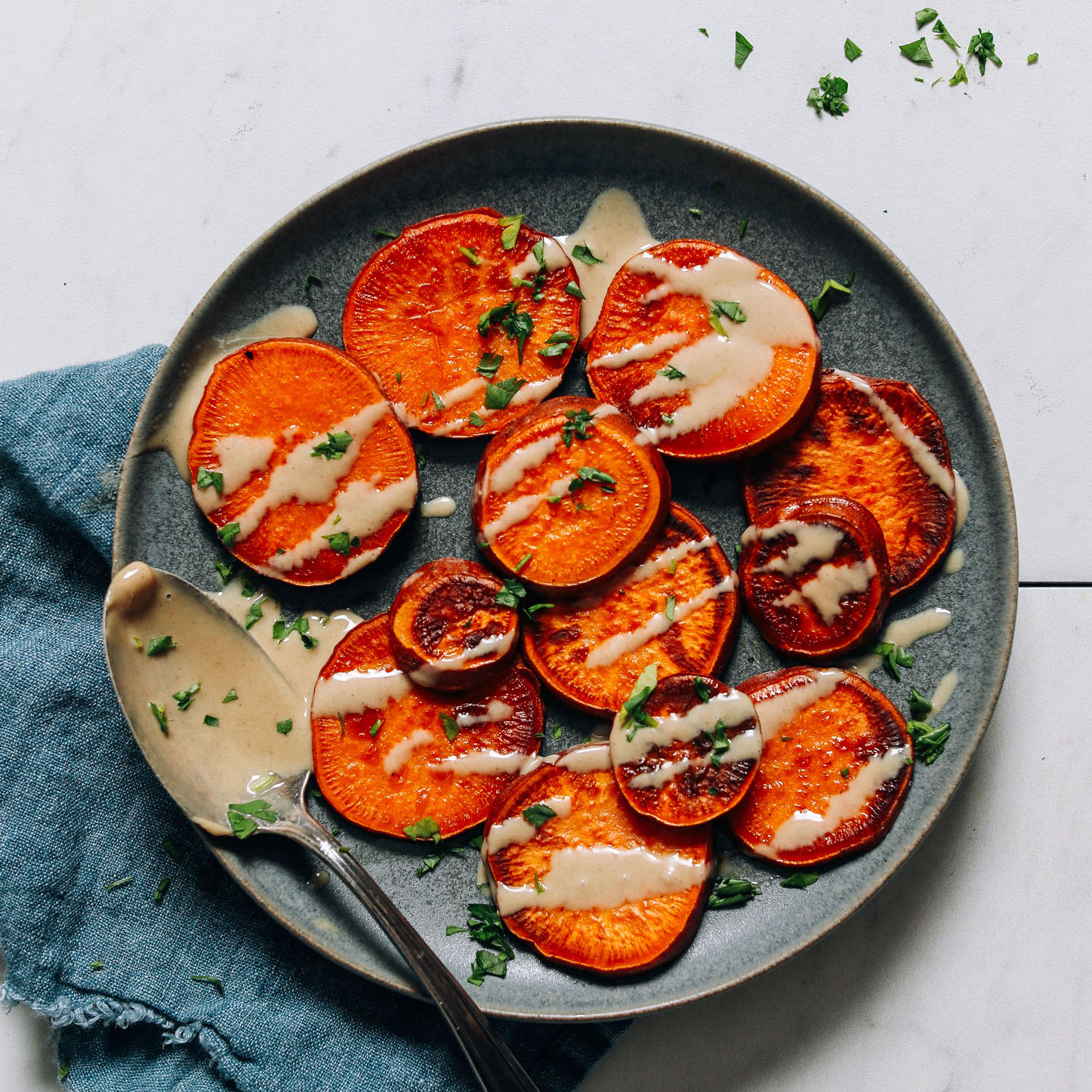 Spoonful of tahini resting on a plate of easy stovetop sweet potatoes