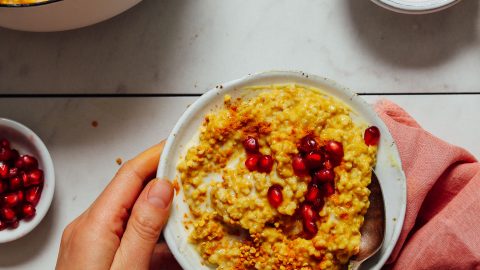 Spoon in a bowl of Cozy Turmeric Porridge topped with pomegranate arrils