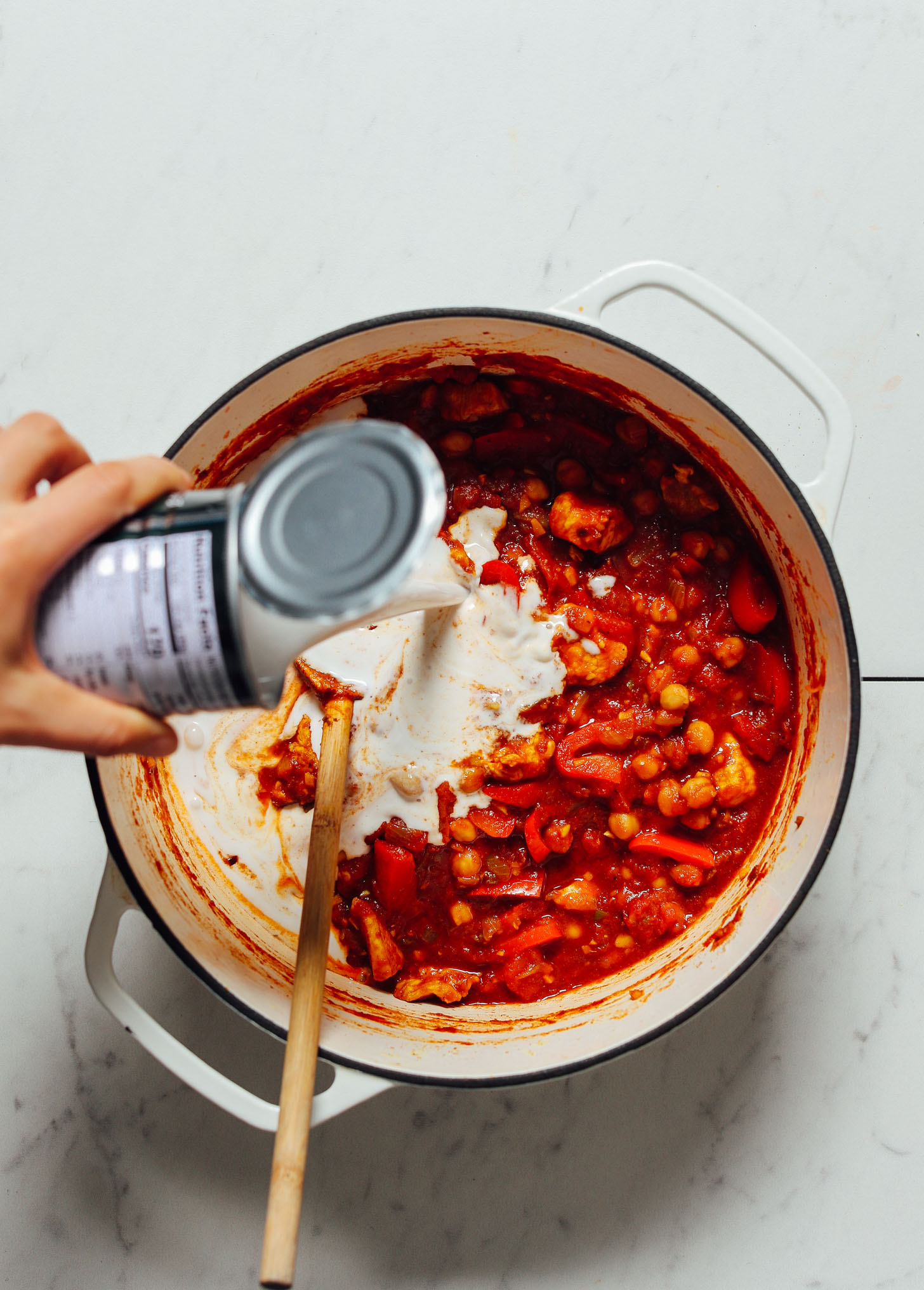 Pouring a can of coconut milk into a pot of Tikka Masala