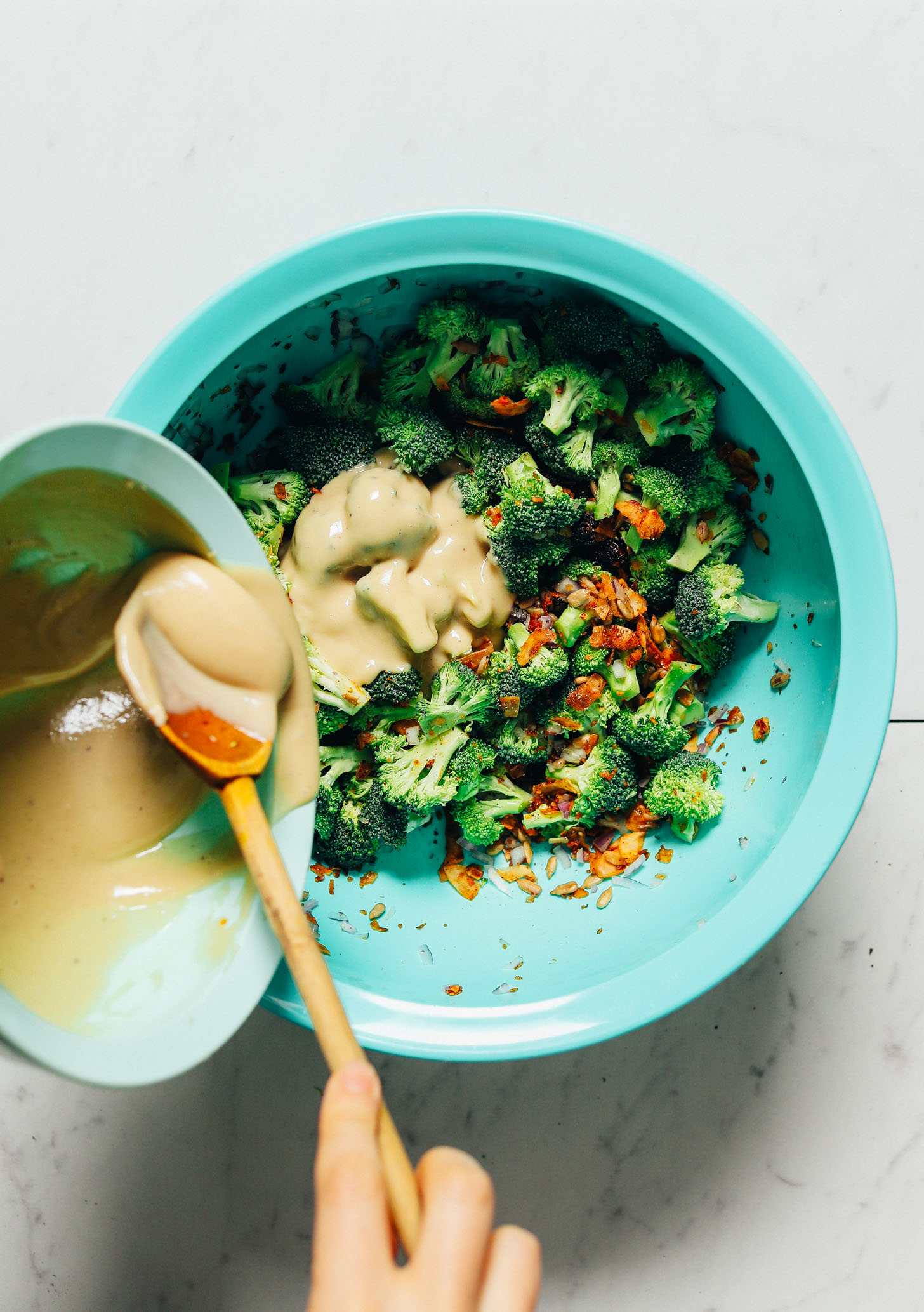 Using a wooden spoon to add cashew butter dressing to our Broccoli Salad recipe