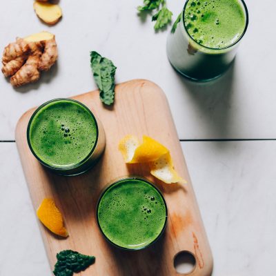 Cutting board with glasses of green juice and ingredients used to make it