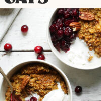 Two bowls of our 25-minute pumpkin steel cut oats recipe with baked cranberries, pecans, and coconut whipped cream