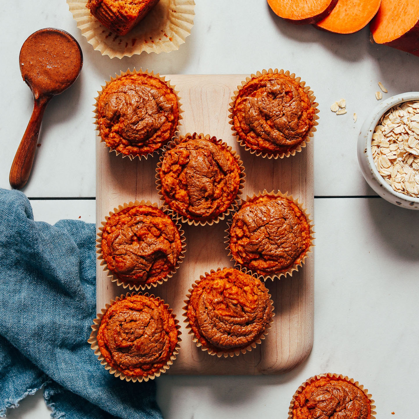 Cutting board filled with Almond Butter Sweet Potato Muffins beside ingredients used to make them