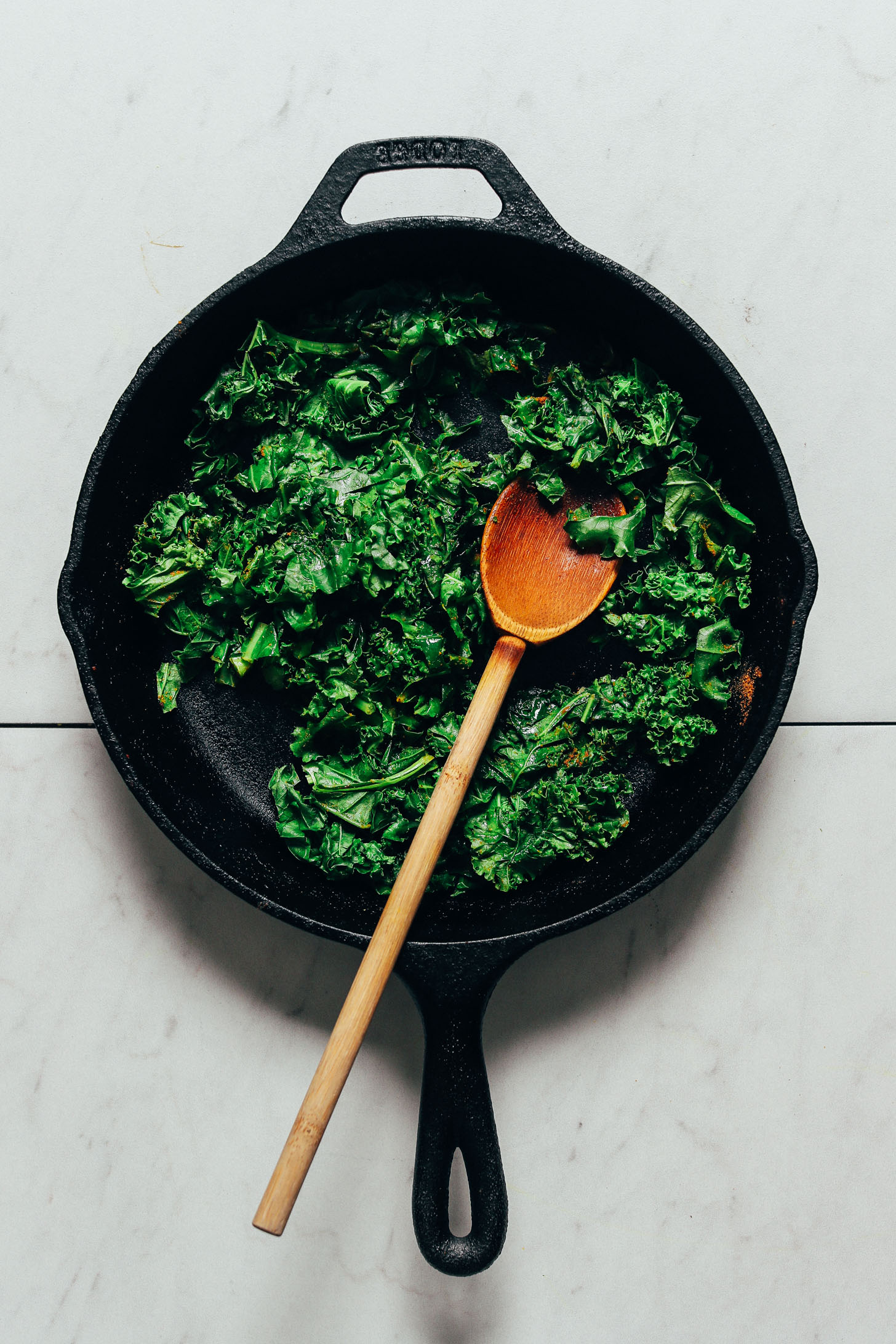 Wooden spoon in a skillet of cooked kale for making our Simple But Good Breakfast Bowl