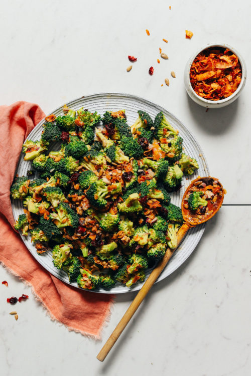 Large plate of our Creamy Vegan Broccoli Salad recipe next to a bowl of coconut bacon