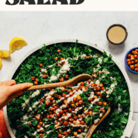 Using wooden serving spoons to toss an easy 15-minute massaged kale salad with chickpeas and tahini dressing