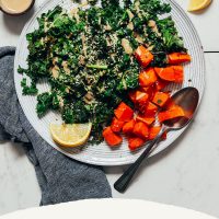 Plate of our Easy Sautéed Kale recipe with tahini dressing, lemon slices, and sweet potato