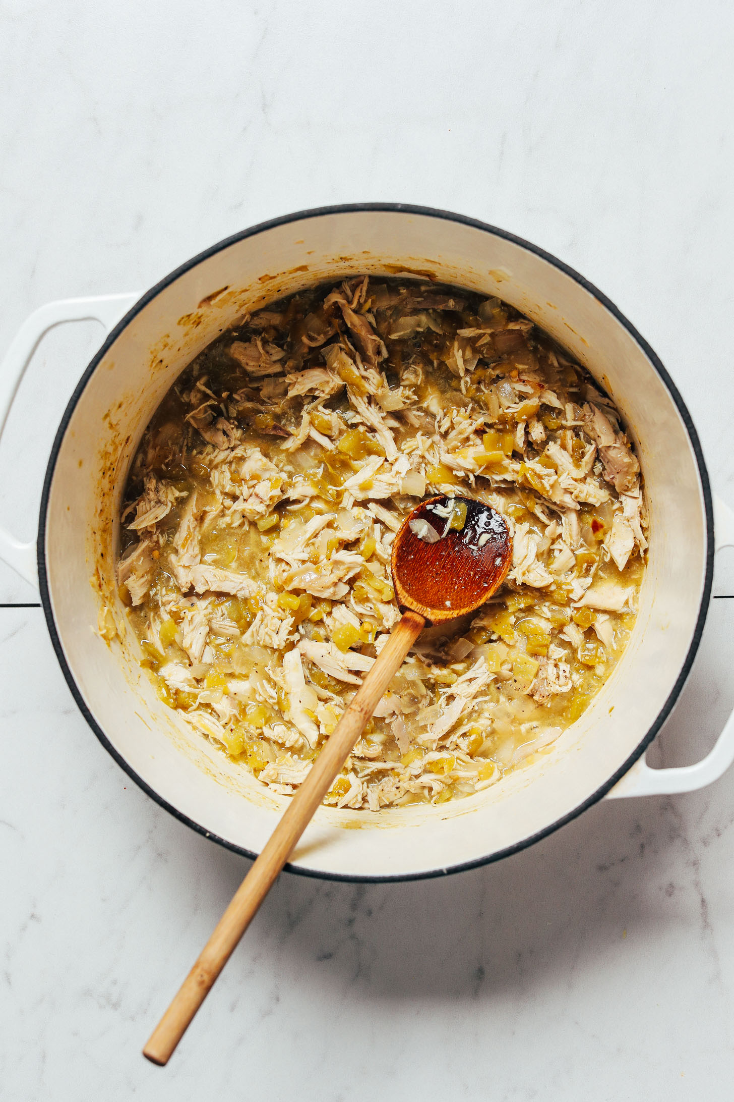 Wooden spoon in a Dutch oven with chicken and green chilies