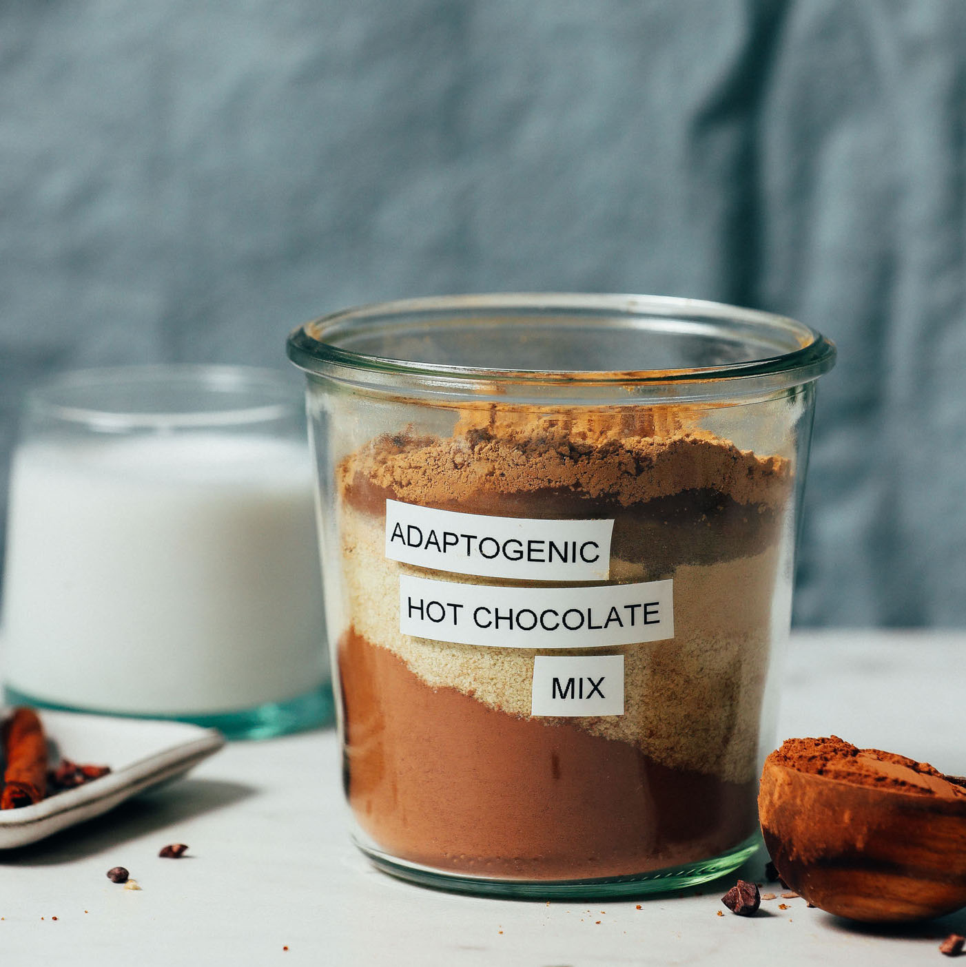 Jar of Adaptogenic Hot Chocolate Mix next to dairy-free milk and ingredients used to make it