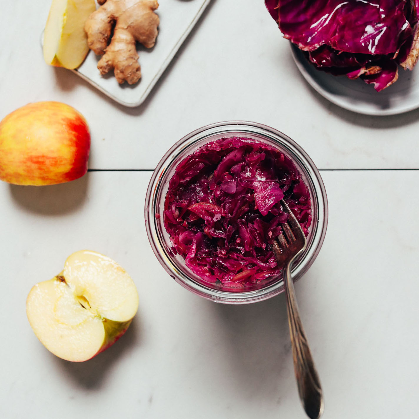 Top down image of a jar of Apple Cabbage Sauerkraut beside fresh ginger and apples