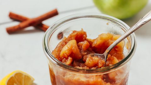 Glass jar of homemade sugar-free applesauce beside ingredients used to make it