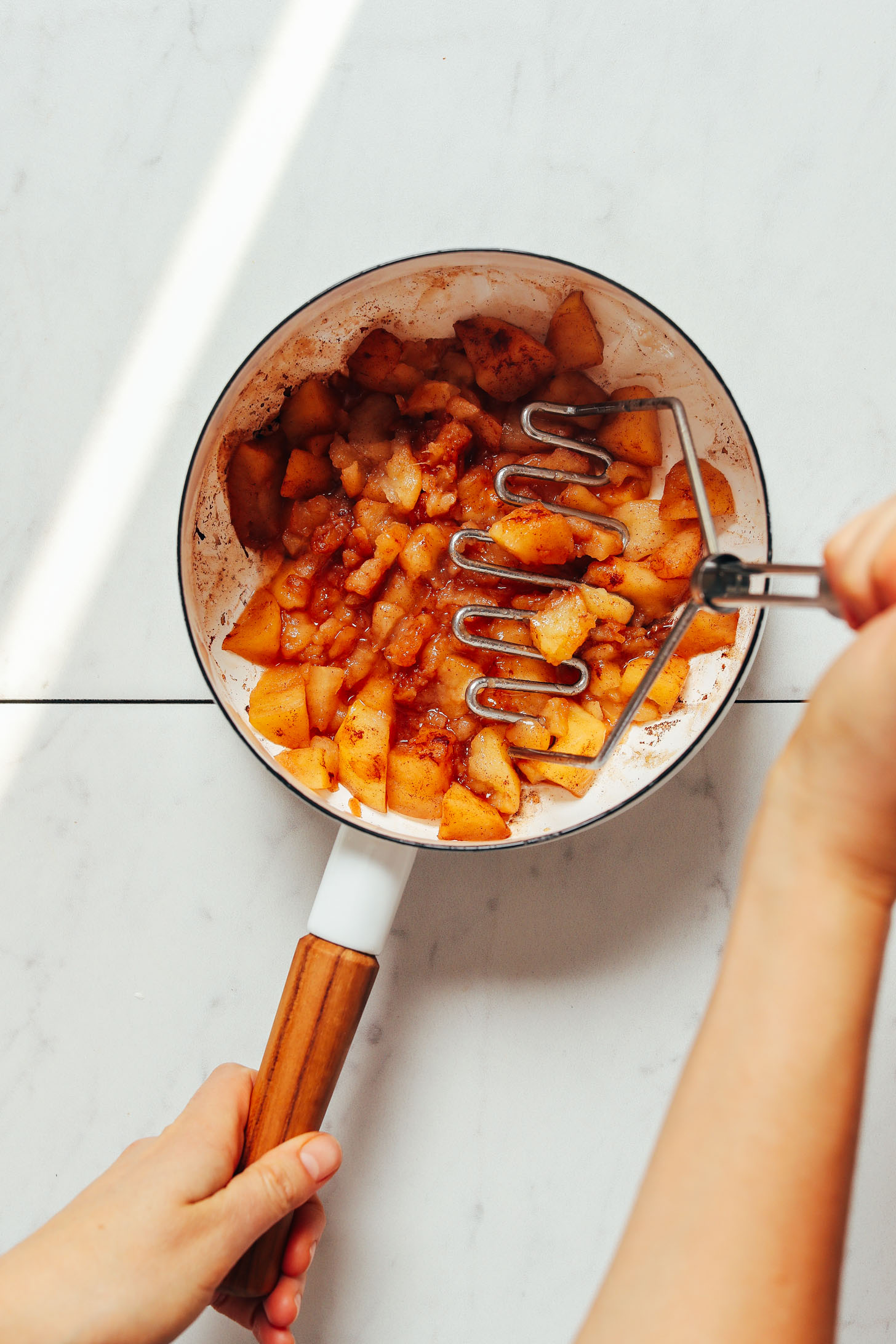 Using a potato masher to smash apples in a saucepan for easy homemade applesauce