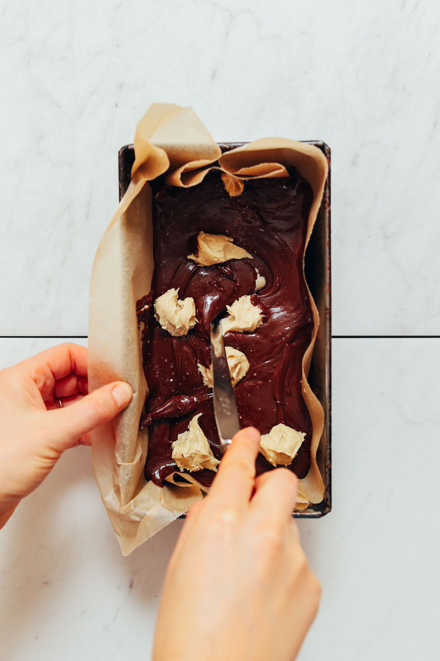 Using a butter knife to add swirls of cashew butter into our Dairy-Free Chocolate Freezer Fudge recipe