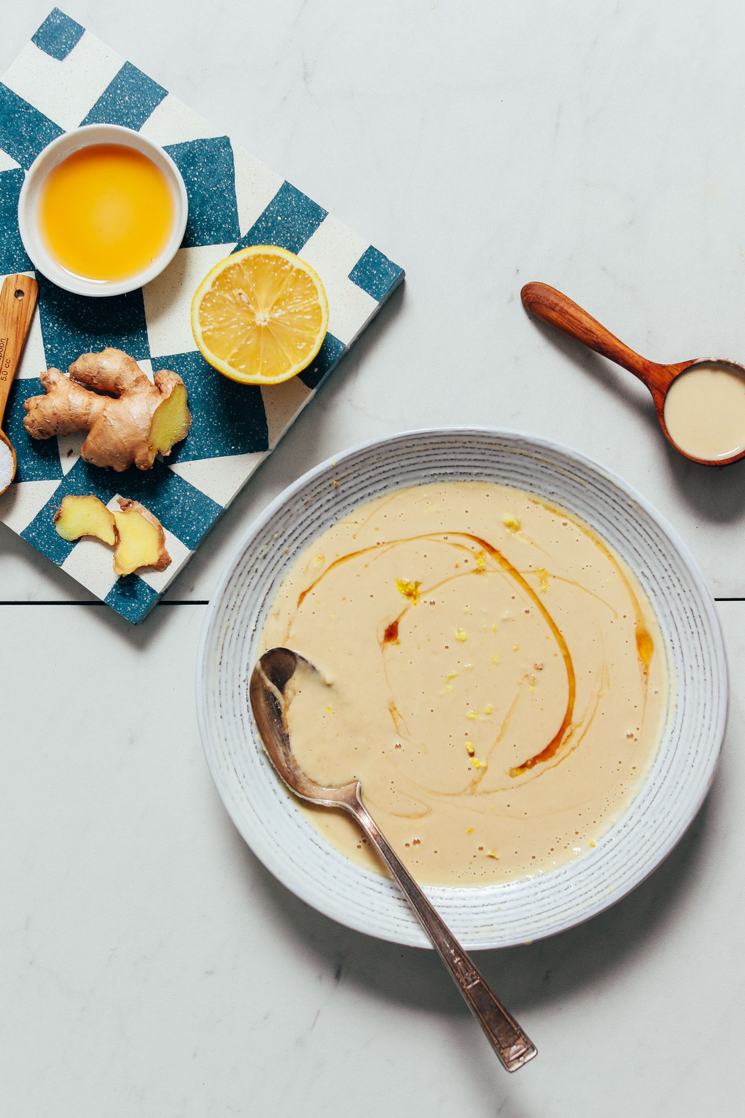 Bowl of our Gingery Lemon Tahini Sauce surrounded by ingredients used to make it