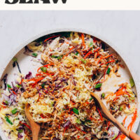 Using salad tongs to toss a crunchy cabbage slaw with sesame ginger dressing