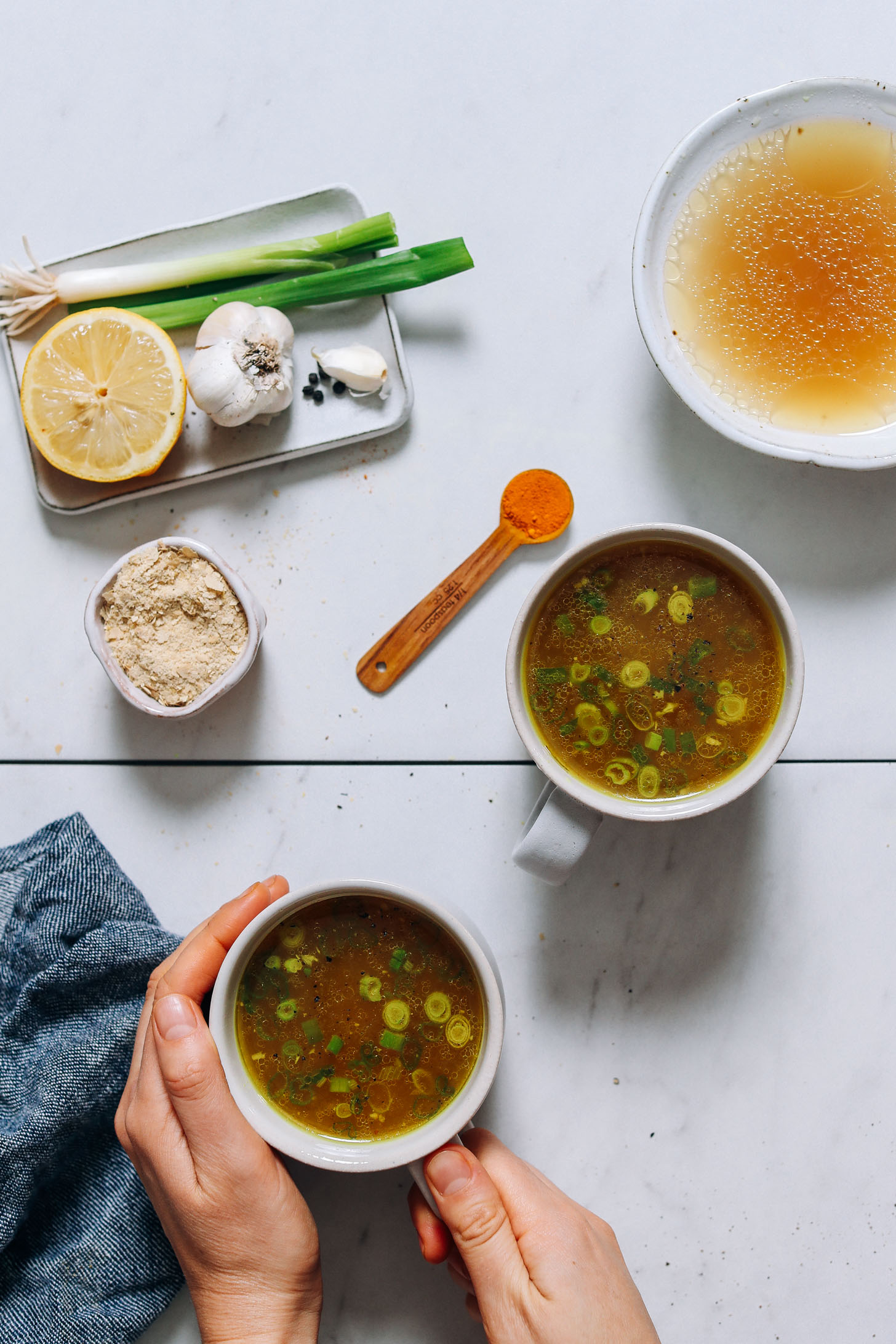Holding the handle of a mug of our Bone Broth Tonic surrounded by ingredients used to make it