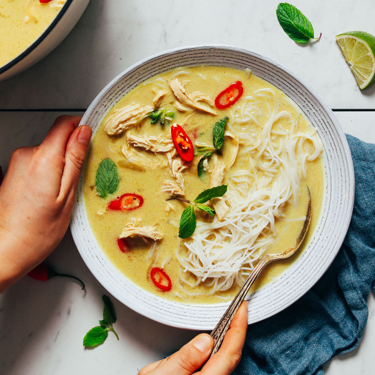 Bowl of Thai-Inspired Chicken Noodle Soup topped with thai chilies and fresh basil