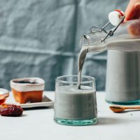 Pouring a glass of Black Sesame Milk from a bottle into a glass