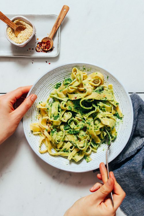 Using a fork to twirl a plate of homemade Gluten-Free Pasta topped with pesto