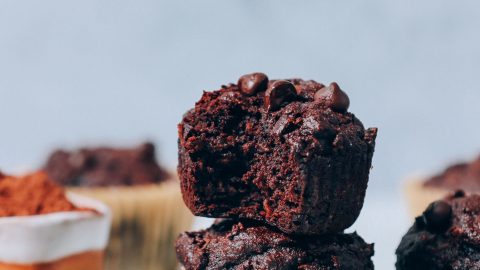 Stack of Banana Chocolate Muffins next to a bowl of cocoa powder