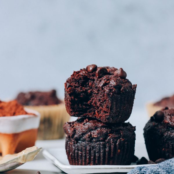 Stack of Banana Chocolate Muffins next to a bowl of cocoa powder