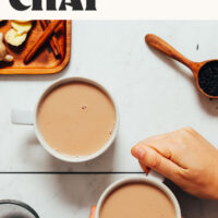 Two mugs of dairy-free masala chai with one being held in hands and text above saying 1 pot and 8 ingredients