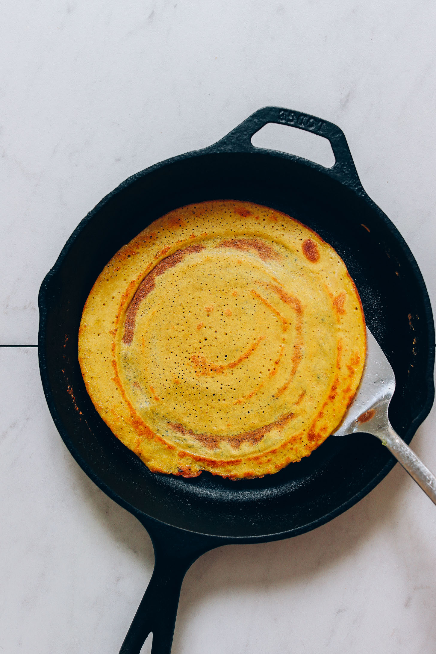 Using a spatula to flip a dosa in a cast iron skillet