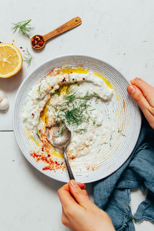 Using a spoon to stir a bowl of dairy-free Yogurt Sauce topped with fresh dill and paprika