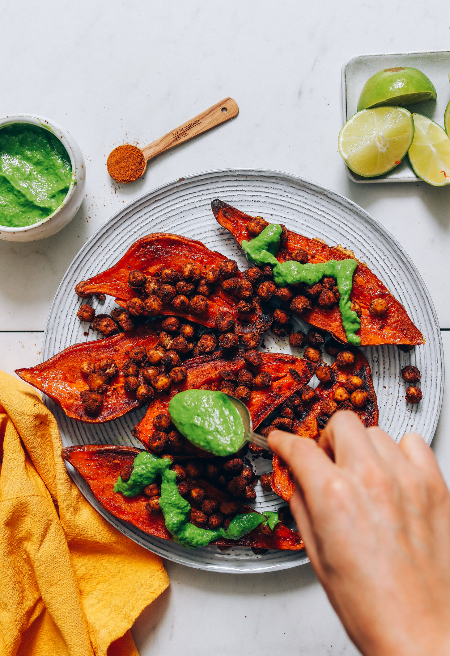 Using a spoon to drizzle green chutney over roasted sweet potatoes and chickpeas