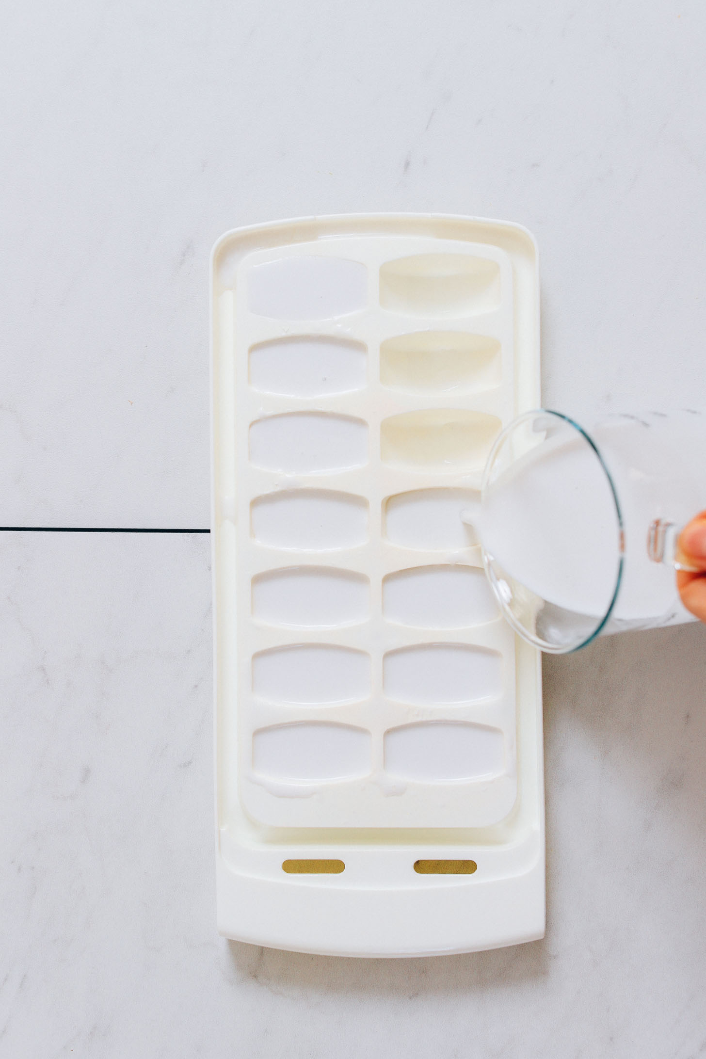 Pouring coconut milk into an ice cube tray to make our Creamy Cold Brew Coffee Smoothie recipe