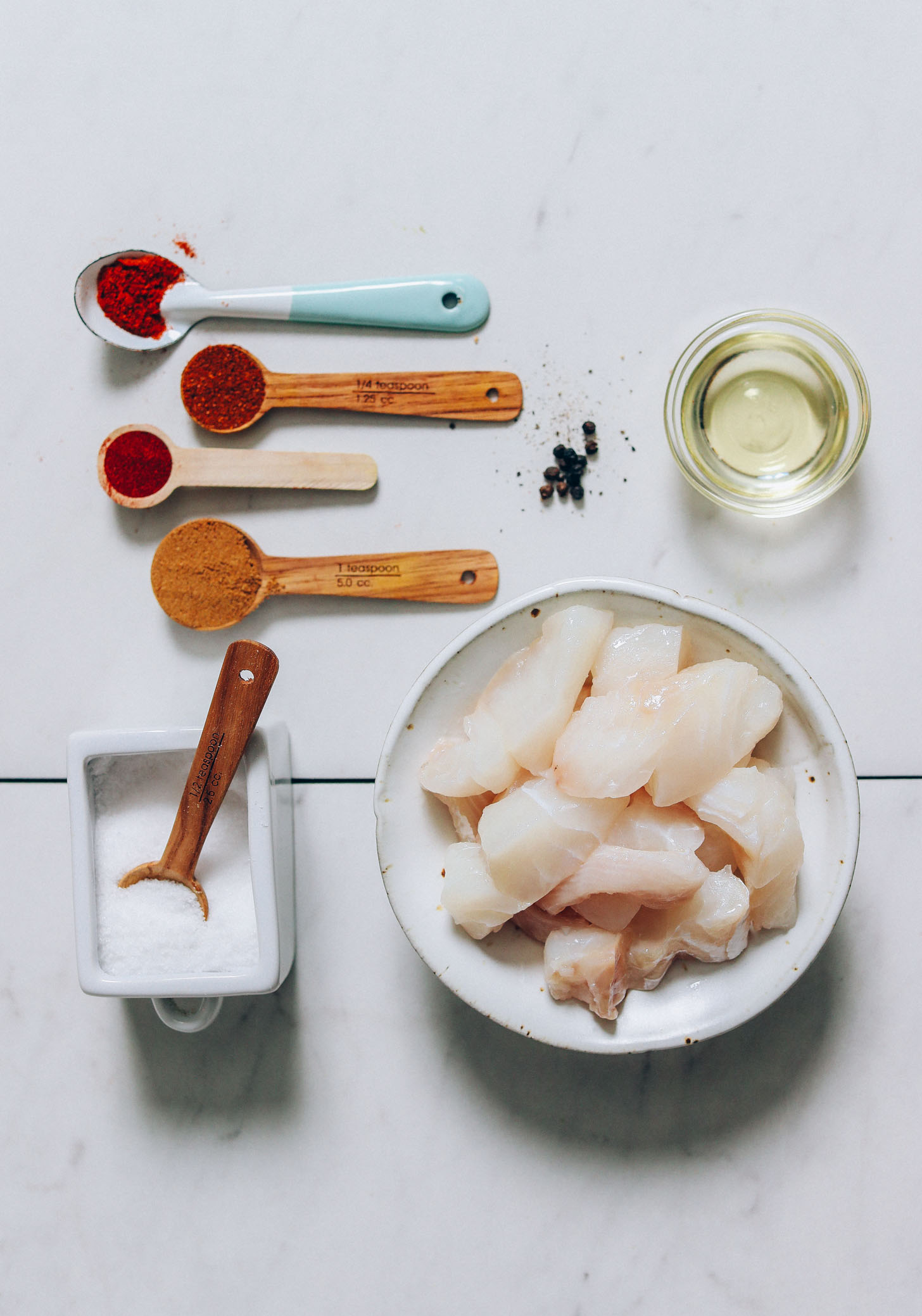 Bowl of cod beside avocado oil, salt, and spices for making our Spicy Fish Tacos recipe