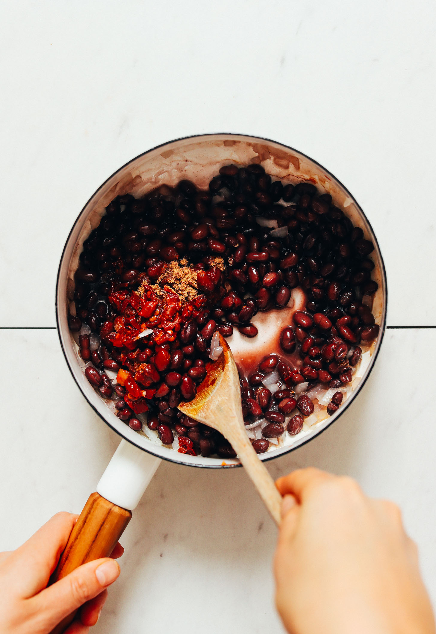 Using a wooden spoon to stir a saucepan of black beans, diced onion, and spices