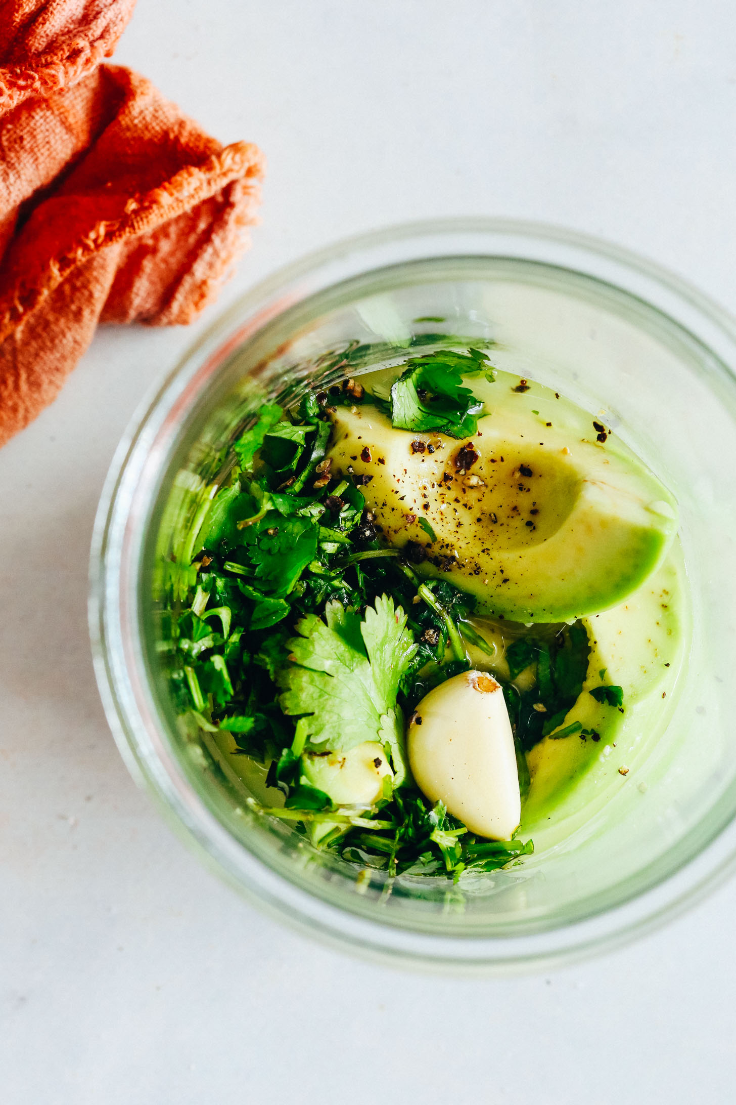 Glass jar with avocado, aquafaba, garlic, cilantro, salt, pepper, and lime juice