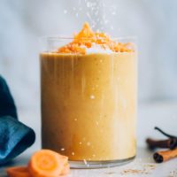 Glass of our vegan carrot cake smoothie topped with shredded carrot and coconut