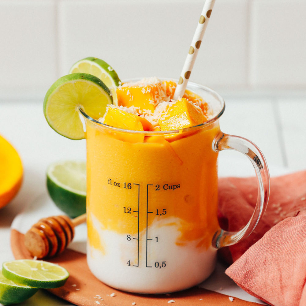 Mango chunks, shredded coconut, and lime slices on a glass of our vegan Mango Lassi