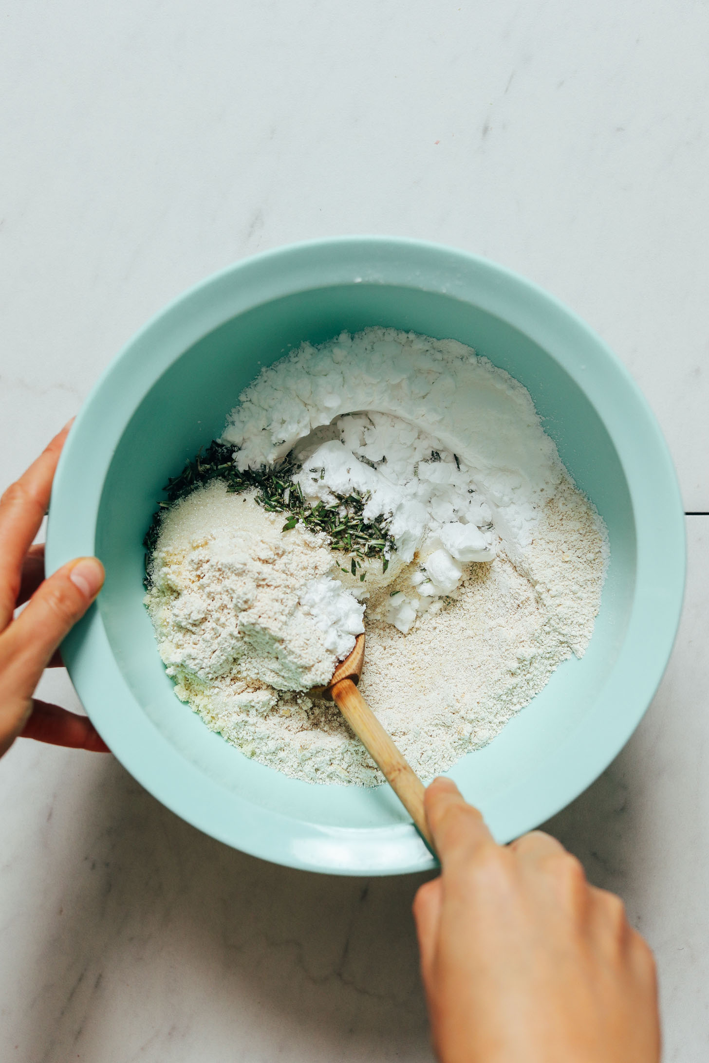 Using a wooden spoon to stir potato starch, almond flour, oat flour, baking powder, sugar, and salt