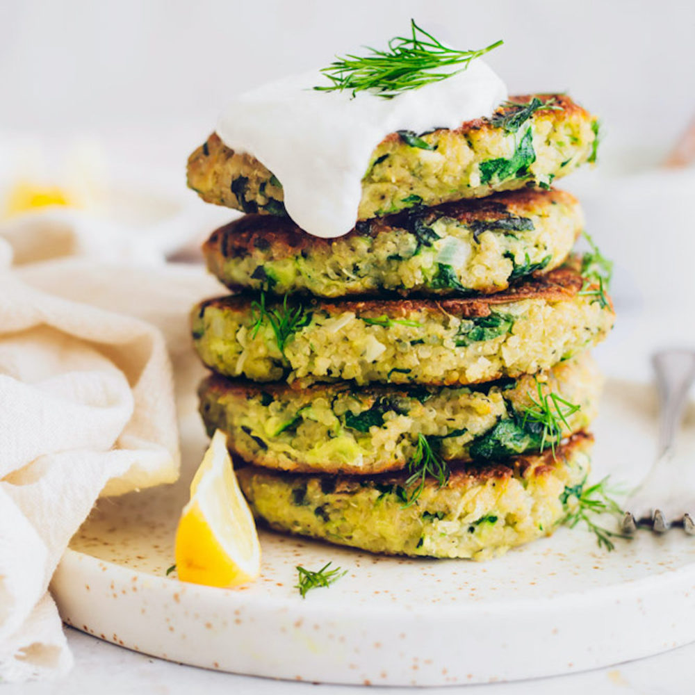 Plate of stacked Vegan Zucchini Fritters topped with dairy-free yogurt and dill