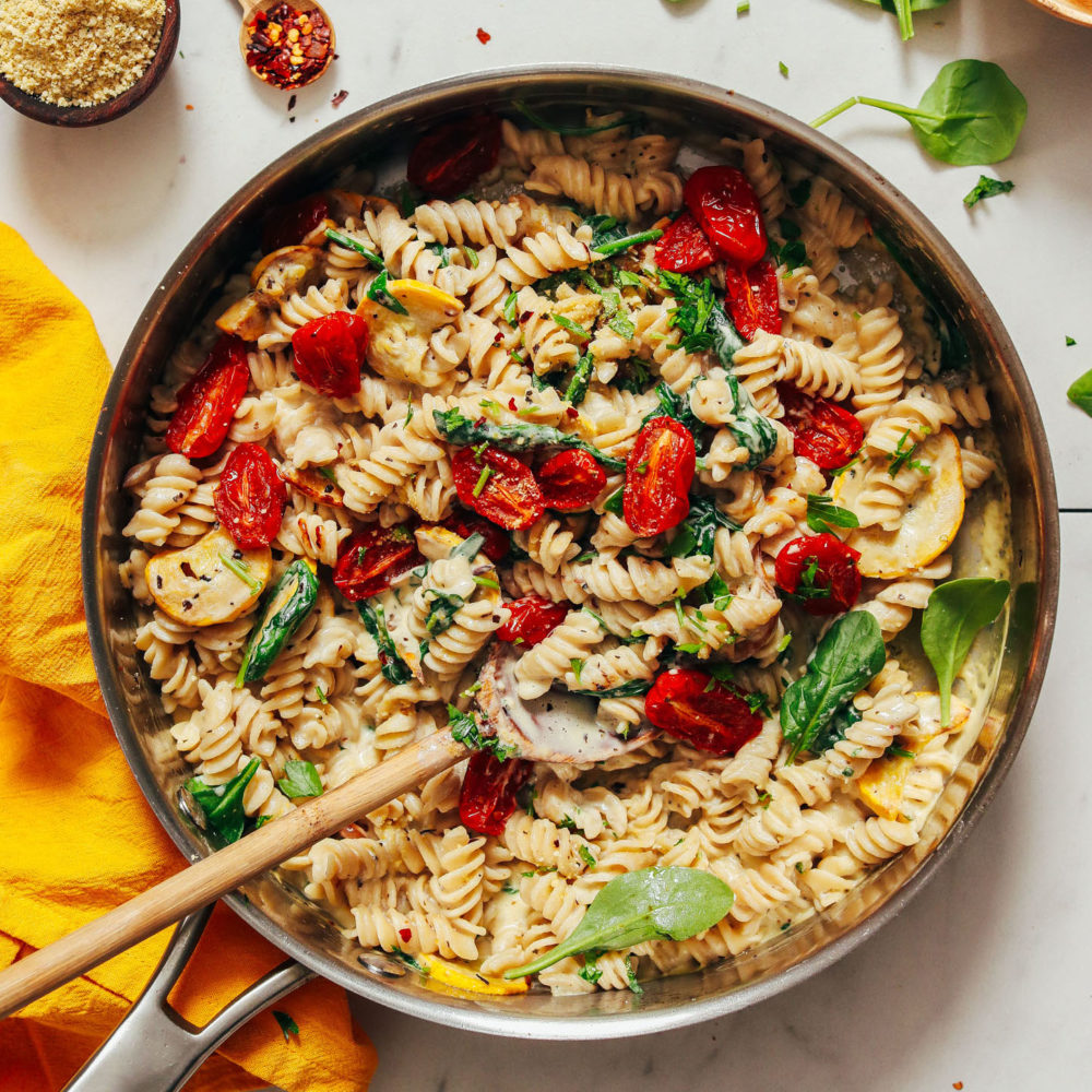 Wooden spoon resting in a pot of Creamy Vegan White Pasta with Summer Vegetables