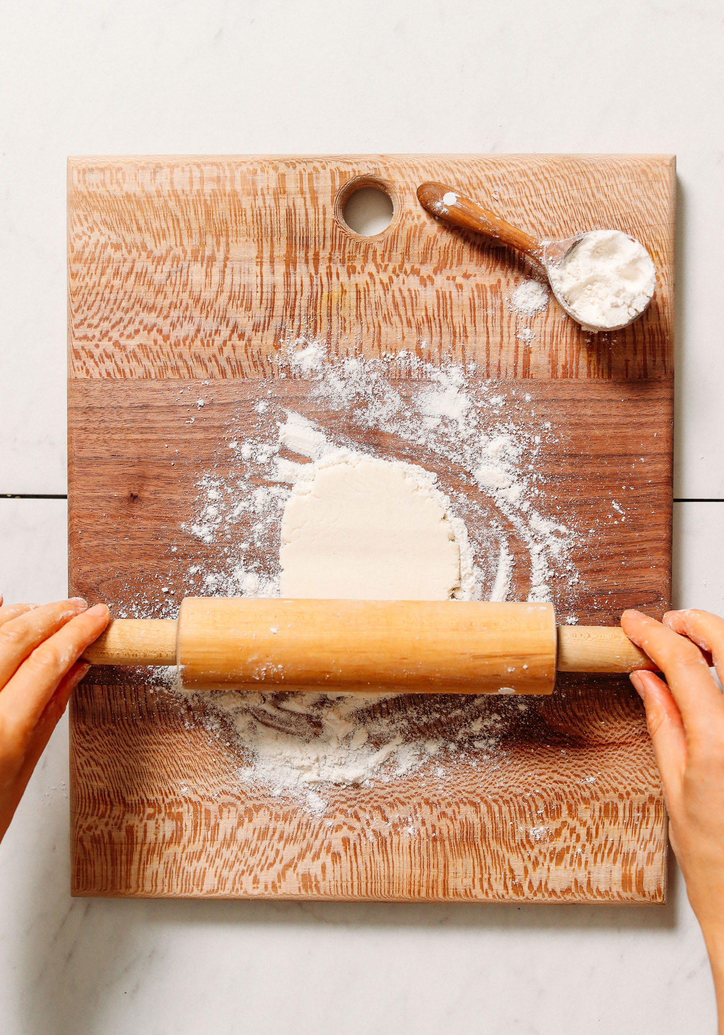Using a rolling pin to roll out naan dough on a floured surface
