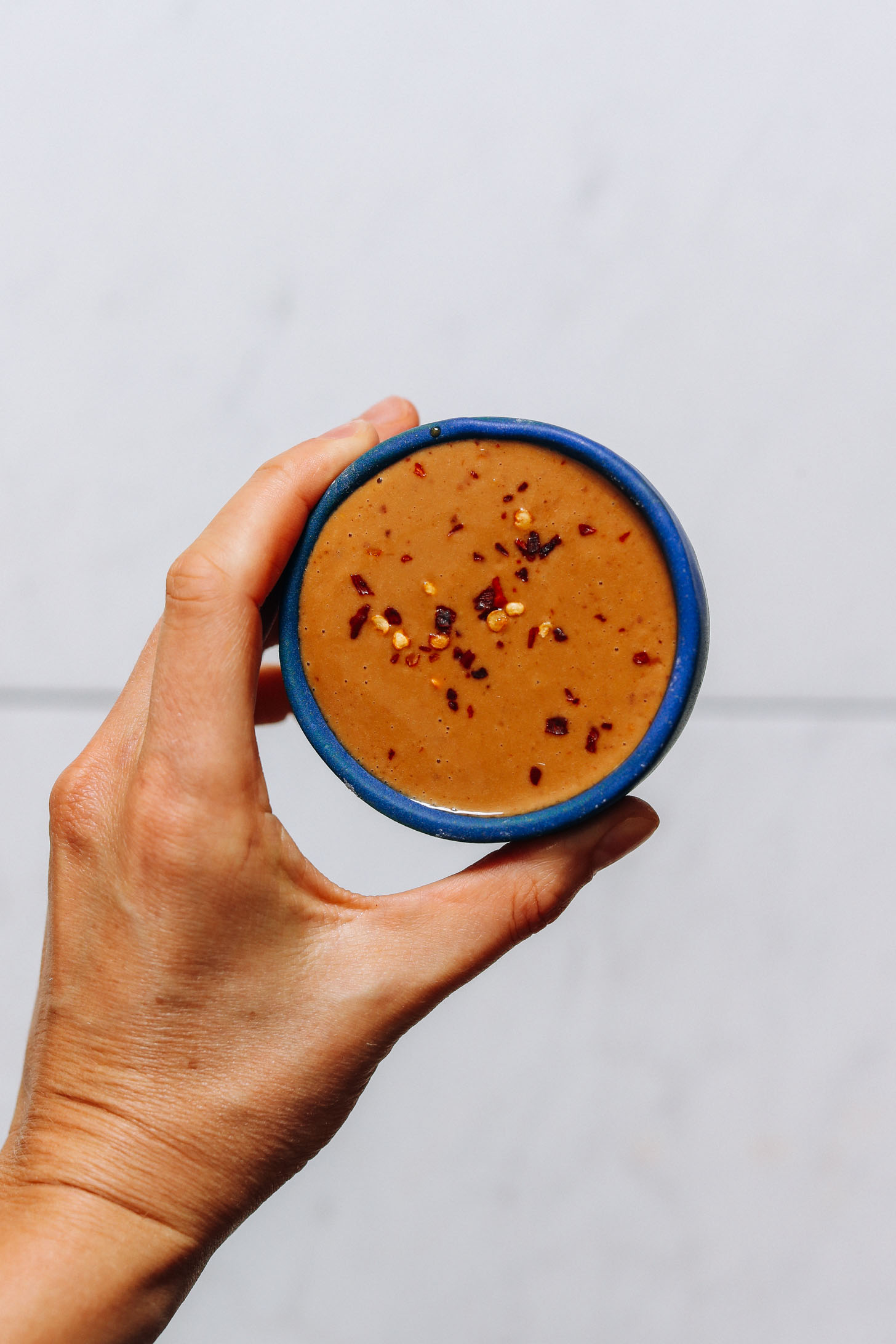 Holding a bowl of homemade peanut sauce topped with crushed red pepper