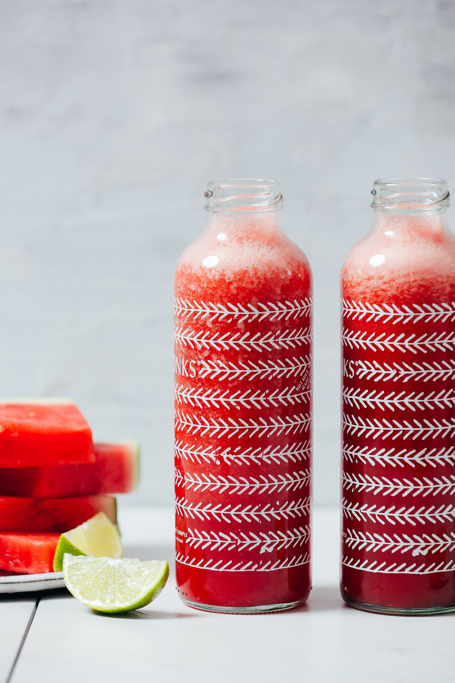 Stack of watermelon slices next to watermelon juice jars and lime wedges
