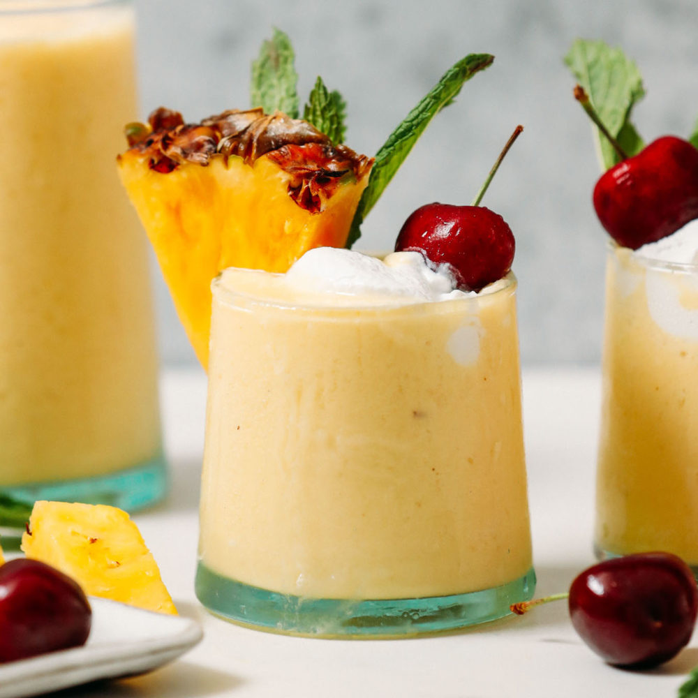 Vegan piña coladas topped with coconut whipped cream, pineapple, mint, and cherries