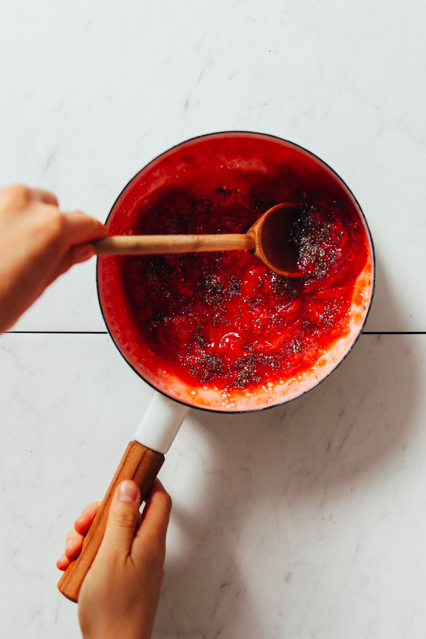 Using a wooden spoon to stir chia seeds into stewed strawberries for homemade compote