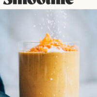 Sprinkling shredded coconut onto a glass of our creamy vegan carrot cake smoothie