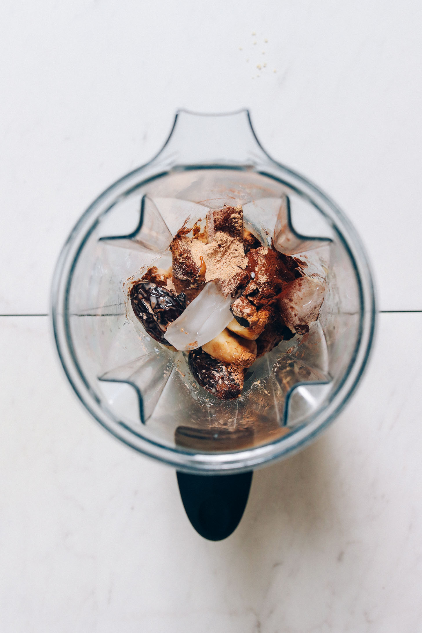 Blender with dates, banana, ice cubes, adaptogenic herbs, and cacao
