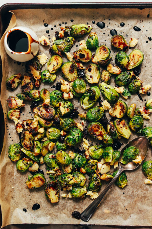 Baking sheet of Crispy Roasted Brussels Sprouts next to a jar of balsamic reduction