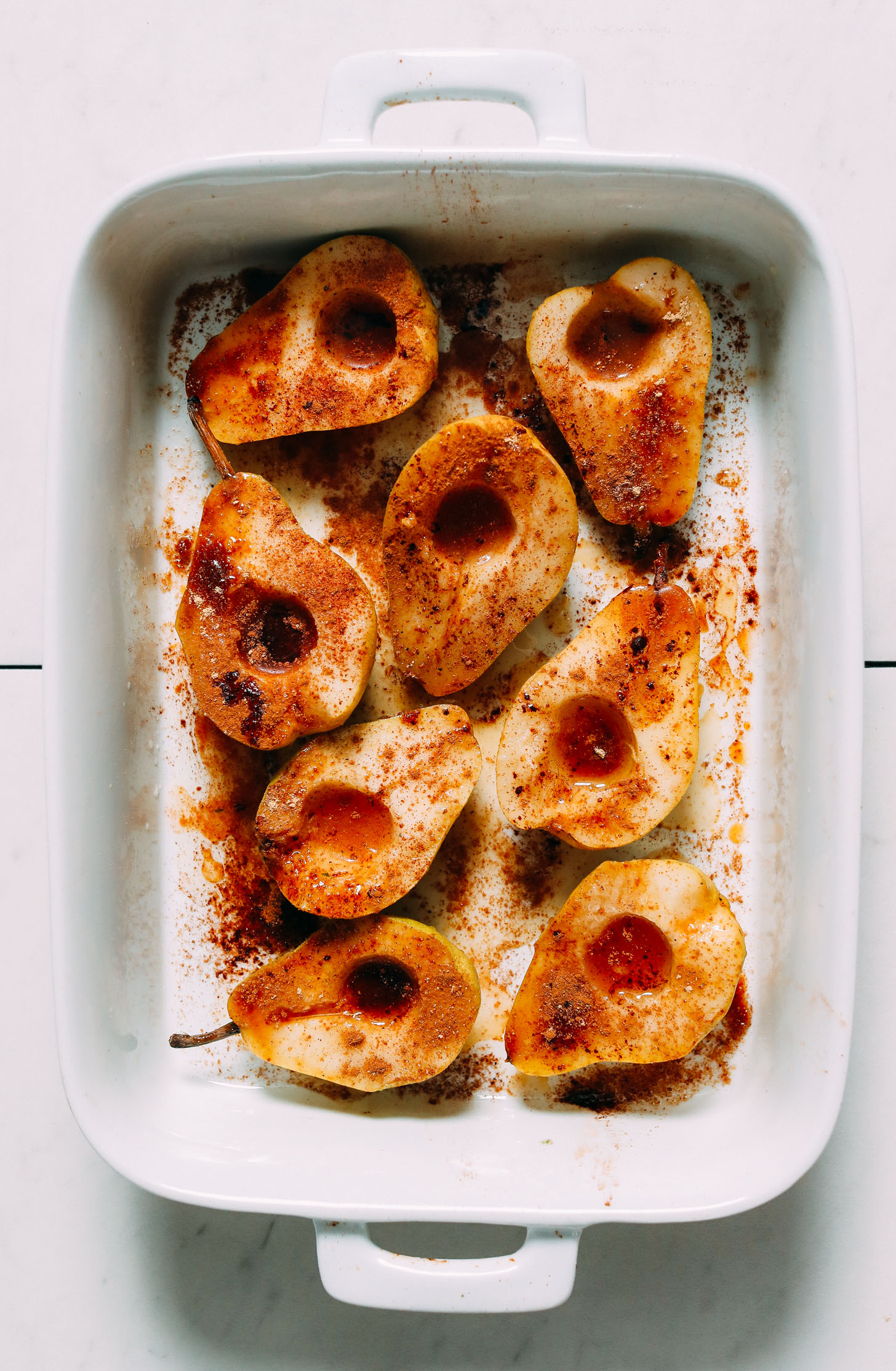 Baking dish of halved pears topped with maple syrup, coconut sugar, and spices
