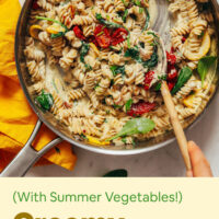 Stirring a pan of creamy vegan white pasta with summer vegetables
