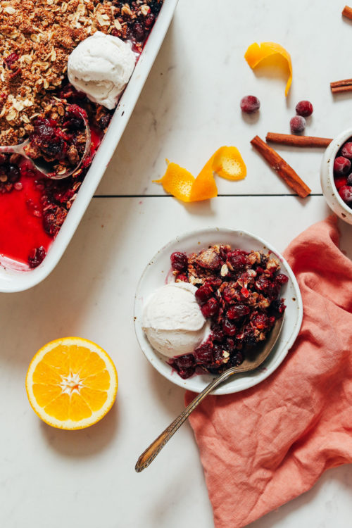 Bowl and baking dish of cranberry crisp with a scoop of vegan ice cream